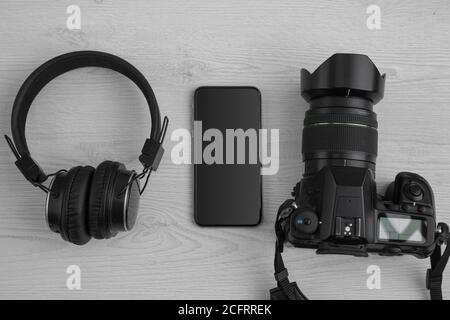 technology, a professional photo camera, a smartphone, wireless studio headphones and a keyboard on a white wooden table. photography - photographer Stock Photo