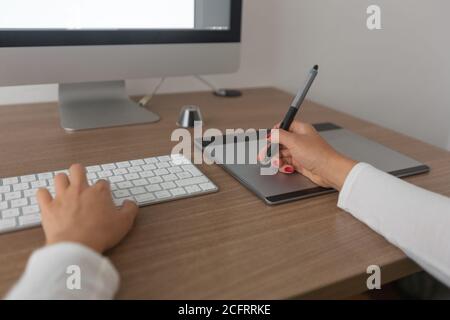 detail of a front view of a woman working on her computer inside an office with a keyboard, a digitizer tablet, glasses and a wooden desk. detail Stock Photo