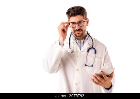 Studio shot of male doctor with serious face holding digital tablet in his hand while standing at isolated white background. Stock Photo