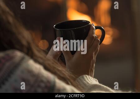 https://l450v.alamy.com/450v/2cfrt9d/black-mug-in-hands-with-lit-fireplace-background-2cfrt9d.jpg