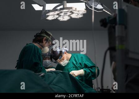 Doctors in an operation, using protections, in the room there is a stretcher and medical instruments Stock Photo