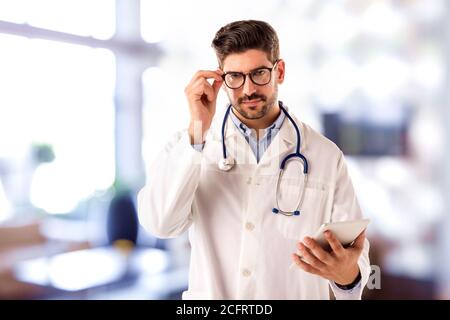 Shot of male doctor holding digital tablet in his hand while standing in hospital’s foyer. Stock Photo