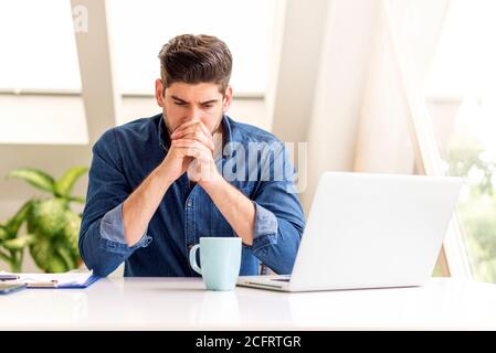 Cropped shot of stressed businessman with hands on his face sitting at office desk and looking thoughtfully. Stock Photo
