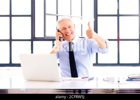 Senior man giving thumbs up while sitting behind his laptop in the office. Stock Photo