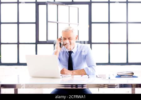 Shot of senior consultant businessman making a call while sitting at office desk and working on laptop. Stock Photo