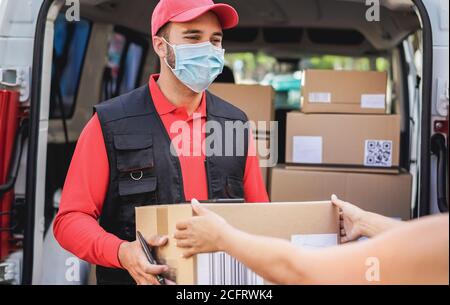 Courier delivering packages with truck while wearing protective face mask for coronavirus prevention - Shipping service and social distance concept - Stock Photo