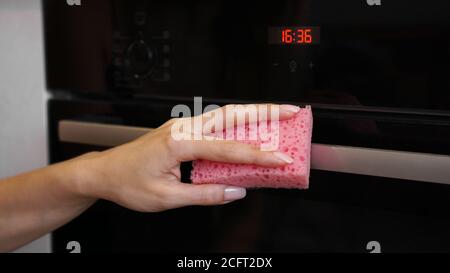 Cleaning the oven outside. A female hand cleans oven panel. Girl polishing kitchen. Stock Photo