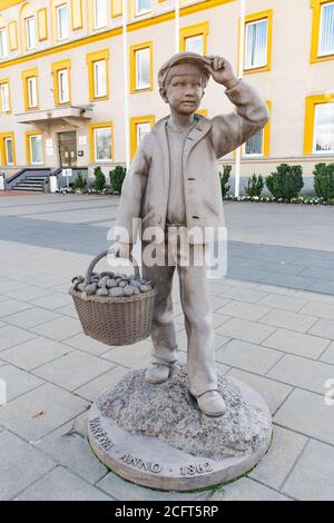 Stone statue of boy with wicker basket full of mushrooms in Varena, Lithuania, vertical Stock Photo