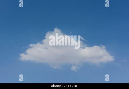 a single small soft and fluffy triangular shaped cumulus cloud in a pure azure blue sky Stock Photo