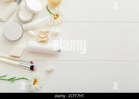 Set white cosmetic products on wooden table with flowers. Beauty makeup brushes skincare hair treatment cosmetic moisturizer skin cream soap lotion Stock Photo