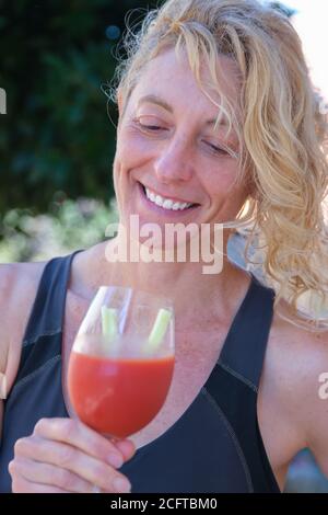 Young mature blonde woman in sportswear outdoor with a glass of tomato juice. Stock Photo