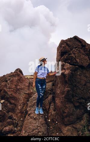 A female wearing a hat standing on huge volcanic rock next to the volcano crater at masaya volcano national park Stock Photo