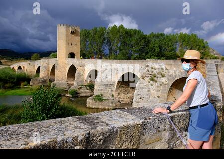 Tourist woman with a hat and a mask and medieval bridge and Ebro river. Stock Photo