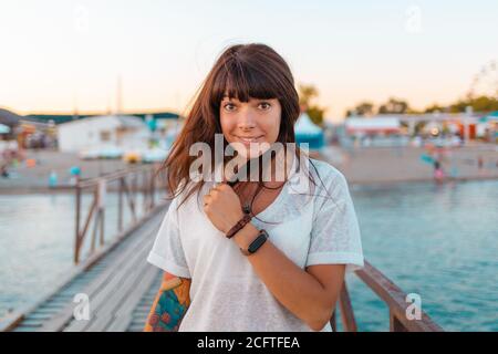 Portrait of smiling woman with a tattoo on her arm. A dock by the sea on the background. Concept of summer vacation. Stock Photo
