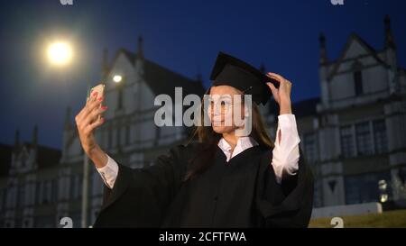 Graduate female student looking at her self in her phone and str Stock Photo