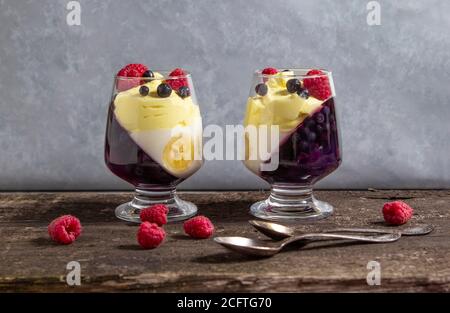 glass jars with dessert (panna cotta, jelly, mousse, pudding) with bilberry and banana layers on wooden rustic table Stock Photo