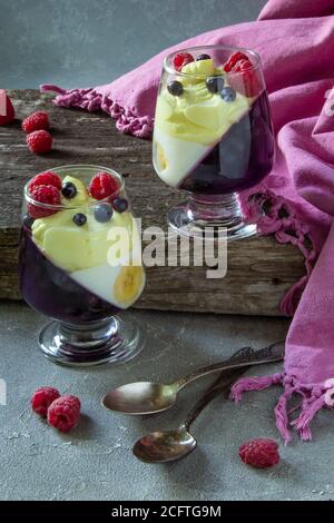 glass jars with dessert (panna cotta, jelly, mousse, pudding) with bilberry and banana layers on wooden rustic table Stock Photo