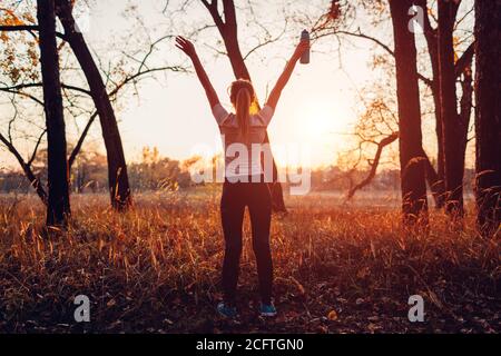 Runner raised arms after workout feeling free and happy succeeded in training. Woman admiring sunset. Stock Photo