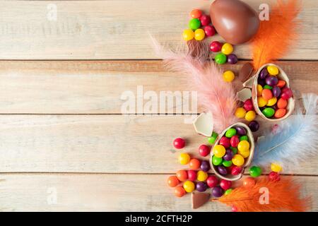 Composition of chocolate Easter eggs and delicate feathers on a light background. Multi-colored sweets for the holiday. Place for text. Stock Photo