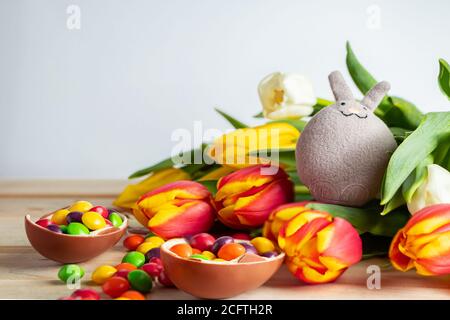 Cute easter bunny and chocolate eggs. Composition for holiday from sweets and tulips. Stock Photo