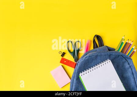 Flat lay student backpack and office supplies on a yellow background. Back to school concept. Place for text. Stock Photo