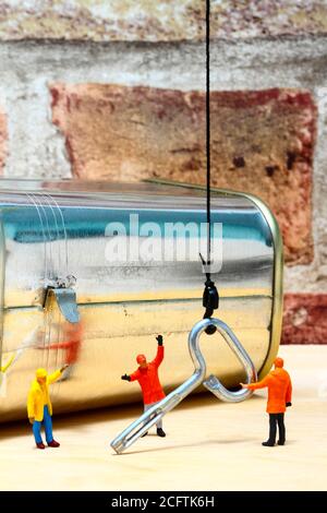 Miniature figure workman using a crane to manoeuver the key for a corned beef tin can opening concept Stock Photo