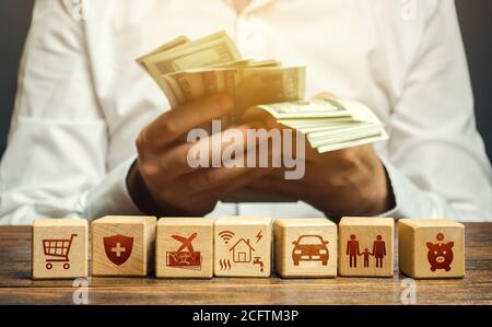A man counts money and blocks with the attributes of family needs. Family budget concept, bills expenses, vacation and transportation. Optimal salary, Stock Photo