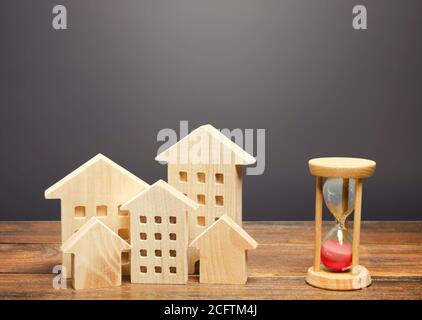 Wooden figures of houses and sand hourglass. Mortgage and loan concept. Temporary rental housing and residence permit. Time to pay taxes and bills. Re Stock Photo