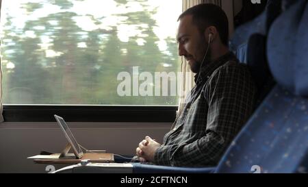 Casual businessman in train with tablet and headphones watching video and smiling. Stock Photo