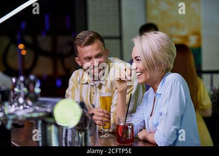 the girl likes the jokes of a stranger, caucasian guy flirt with blond girl in a pub or bar Stock Photo