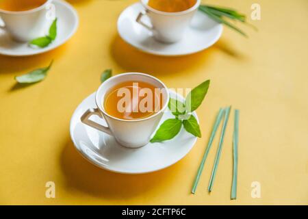 Herbal green tea with lemongrass in glass cup with fresh limes. Top view of three white cups of Lemon Grass Drink on a Yellow Background. Stock Photo