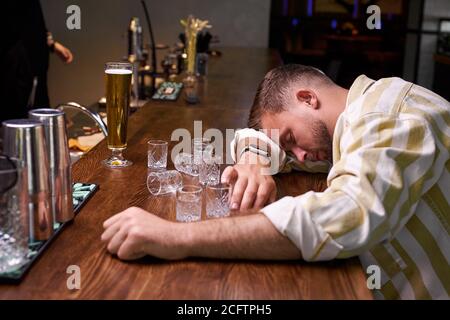 A drunk man sits at a table with a glass in his hands and tries to put ...