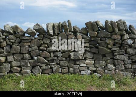 3 - Plain abstract background texture of dry stone wall. Close up of random mix of stone brickwork. Cloudy background and plants in foreground. Stock Photo