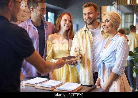 here you are. pleasant blissful group of friends getting the menu in cafe, they are served by a polite affable waiter Stock Photo