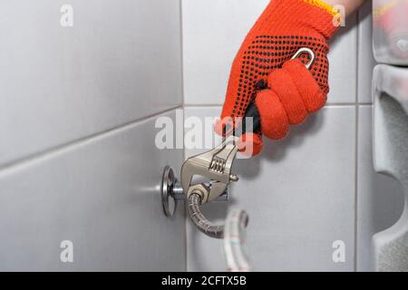 Plumber installs of a toilet hose in a hard-to-reach place with an adjustable wrench. Stock Photo