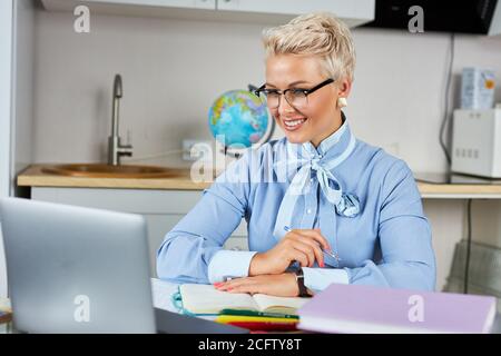 blonde caucasian female young school teacher using webcam at home, virtual teaching concept, giving remote class online lesson by zoom conference call Stock Photo