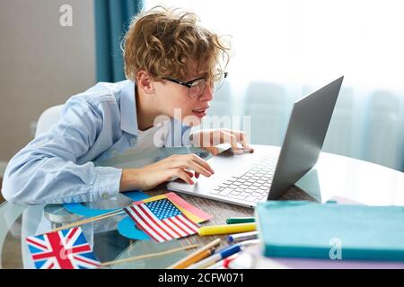 teen schoolboy prepares a presentation, writes a report, types on a laptop keyboard. do homework at home, in bedroom Stock Photo