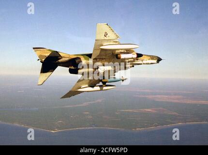 1976 - An air-to-air right underside view of an F-4E Phantom II aircraft equipped with an SUU dispenser on right wing, Pave Tack center mounted and an LGB-10 Mark 84 on left wing. Stock Photo