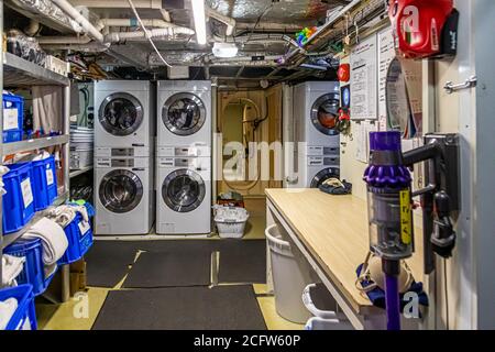 Four washing machines are stacked in pairs in the laundry room of the expedition yacht True North, East Nusa Tenggara, Indonesia, with blue laundry baskets filling the shelves alongside. Stock Photo