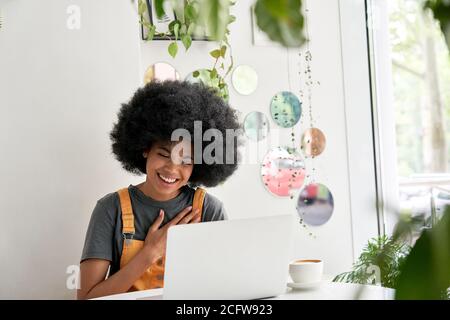 Happy African lady student using laptop laughing sitting at table in cafe. Stock Photo