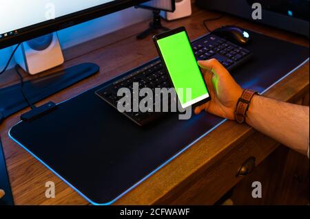 Unrecognisable male operating phone sat at computer desk at home. green screen Stock Photo