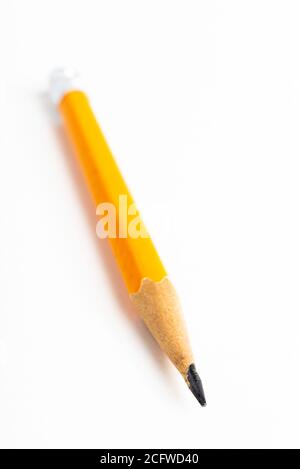 A close-up or macro shot with selective focus of a sharpened classic yellow-orange hexagonal pencil stub set on plain white paper. Stock Photo