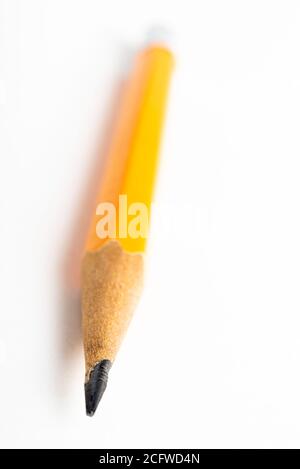 A close-up or macro shot with selective focus of a sharpened classic yellow-orange hexagonal pencil stub set on plain white paper. Stock Photo