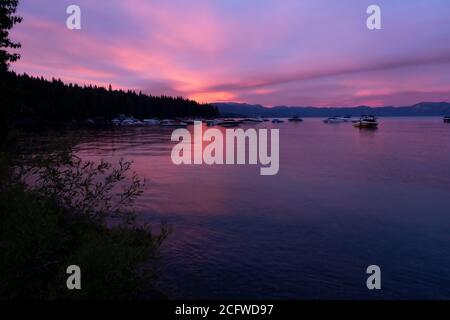 Radiating sunset over Lake Tahoe, foliage and deep water foreground, boats, forest, mountains background Stock Photo