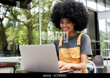 Happy African woman student using laptop sitting at table in outdoor cafe. Stock Photo