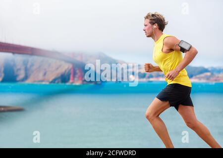 Runner man listening to music during run cardio workout. Running athlete using app on smartphone armband and earphones. Sporty fit young jogger Stock Photo