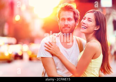 Young happy interracial couple in sunshine flare enjoying sunset relaxing having fun on urban city street in New York city, USA. Playful multiracial Stock Photo