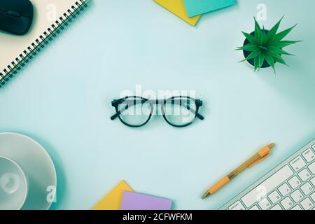 Glasses at Center and Office Supplies as Keyboard,Pen,Sticky Note,Office Plants,Spiral Notebook,Mouse,Coffee Cup on Modern Clean Creative Office Desk Stock Photo