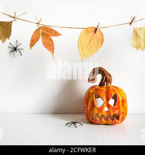 Halloween ceramic pumpkin jack lantern and floral garland on table wall background Stock Photo