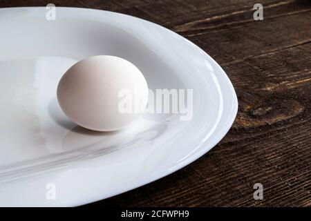 white chicken egg on a white ceramic plate on a brown wooden table Stock Photo
